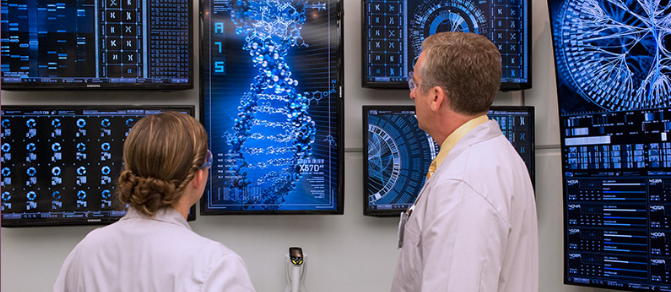 A picture of two researchers wearing lab coats and staring at a glowing blue picture of (poorly-drawn) DNA on the wall. The research on the left is short and has long blonde hair pulled into a pony tail. The researcher on the right has short grey hair.